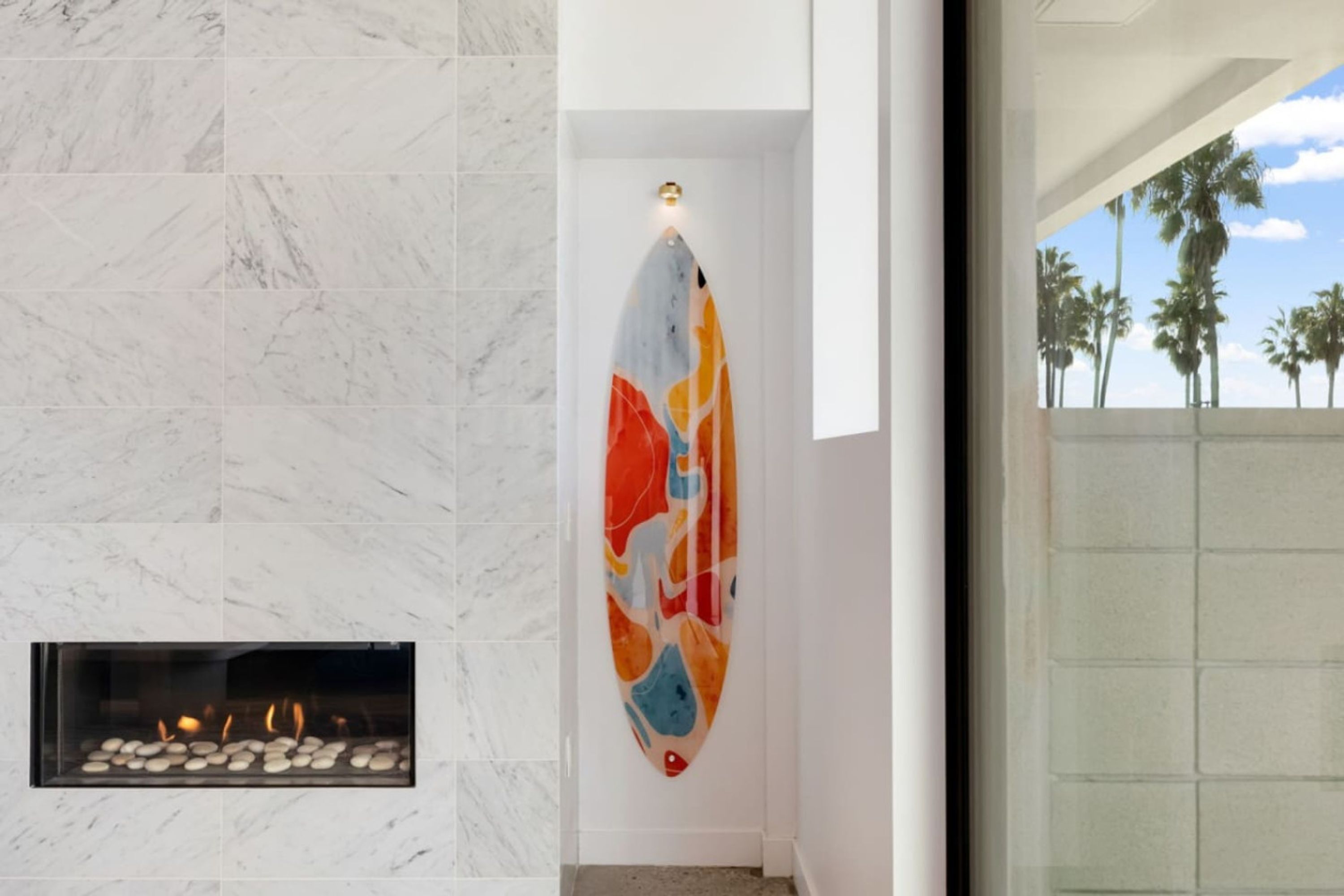 A modern interior with a marble wall, a colorful abstract artwork, and a fireplace with stones.