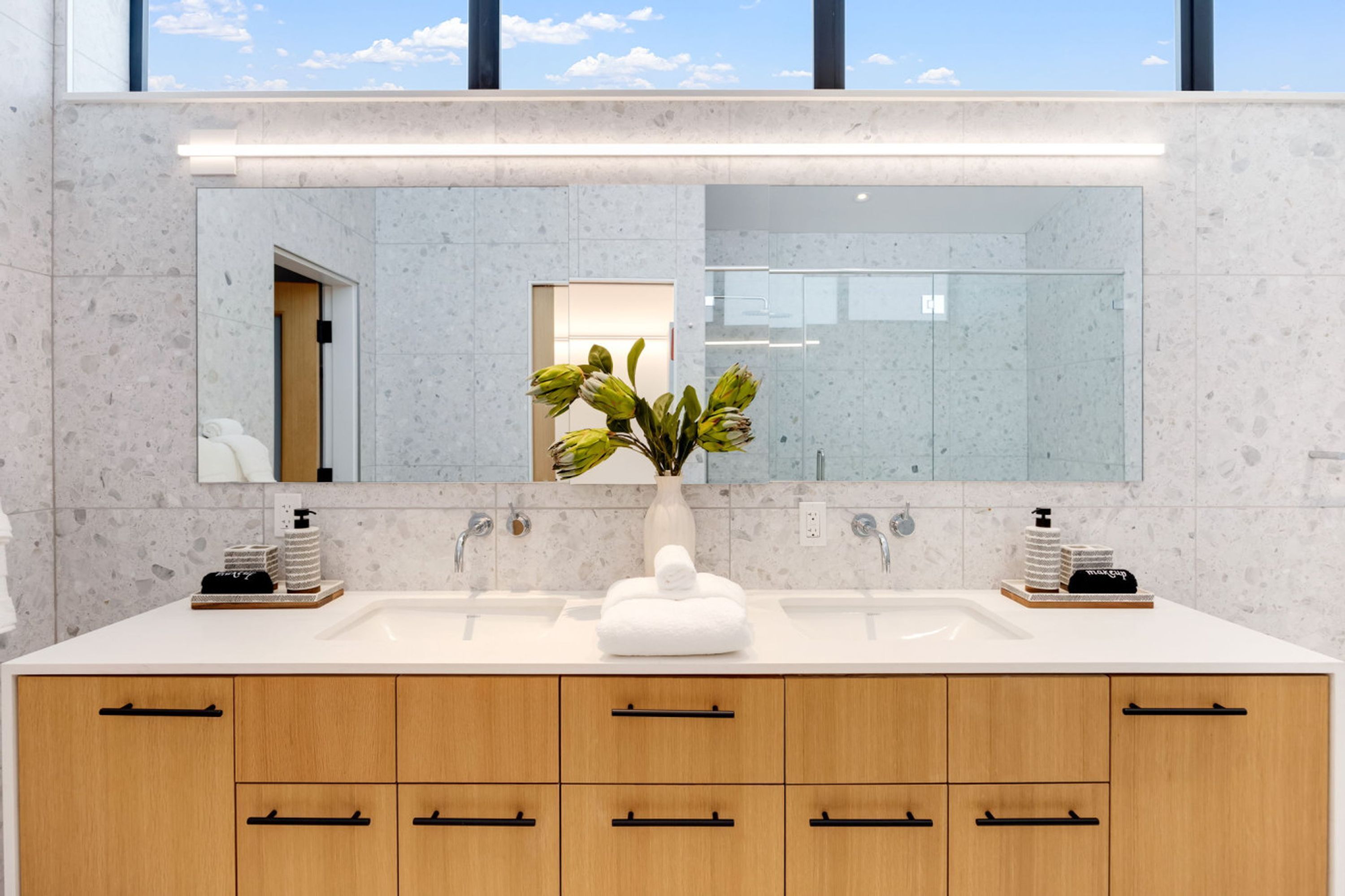 A modern bathroom with a large mirror, two sinks, and wooden cabinets.