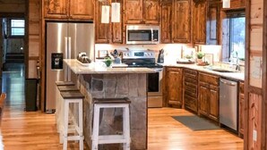 A spacious kitchen with wooden cabinets, a central island, stainless steel appliances, and pendant lighting.