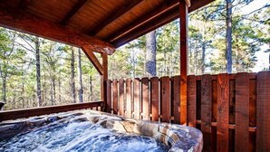 A hot tub with a wooden deck and railing, surrounded by a forested area.
