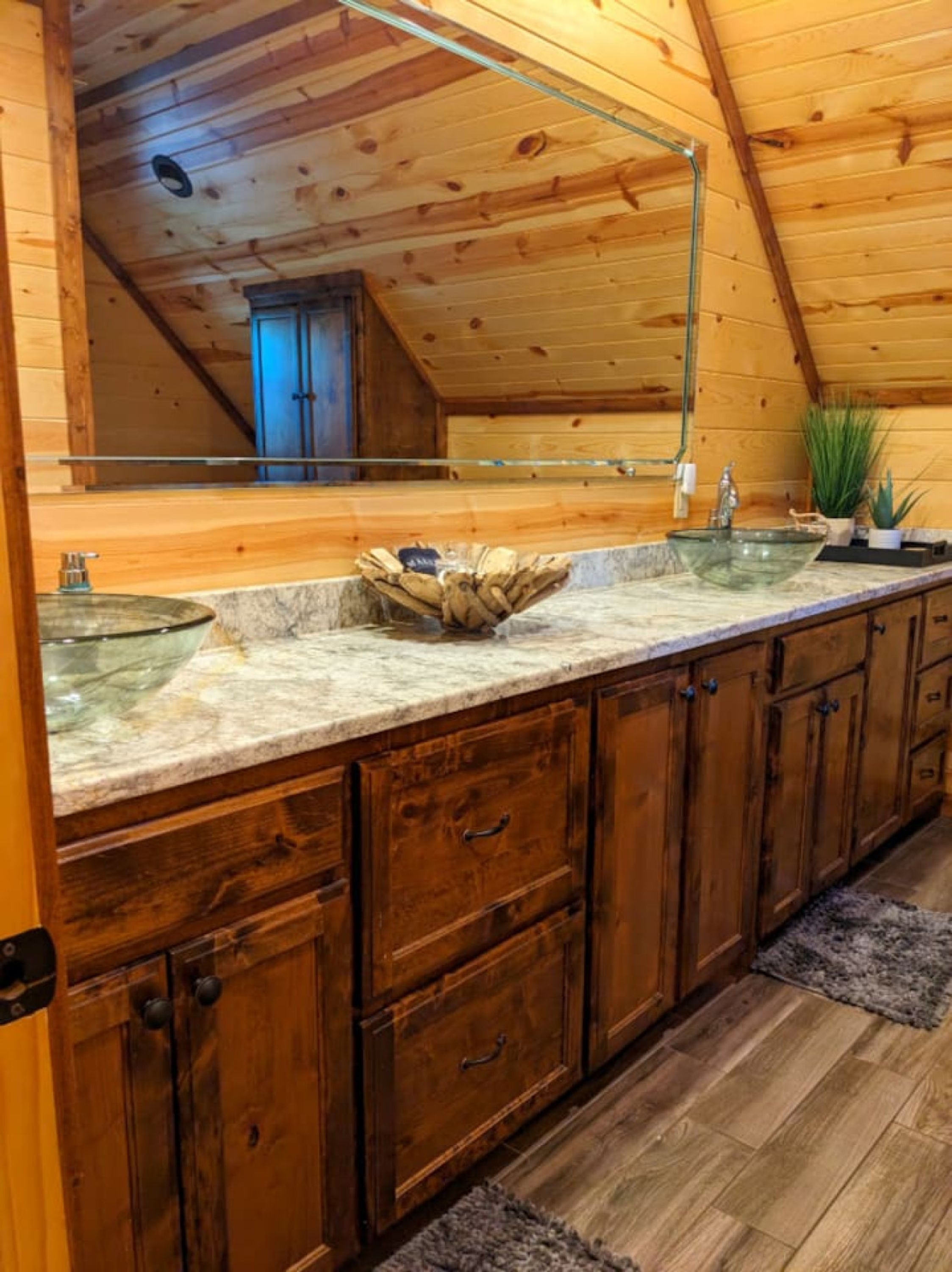 A wooden cabin bathroom with a large mirror, two sinks, and wooden cabinets.