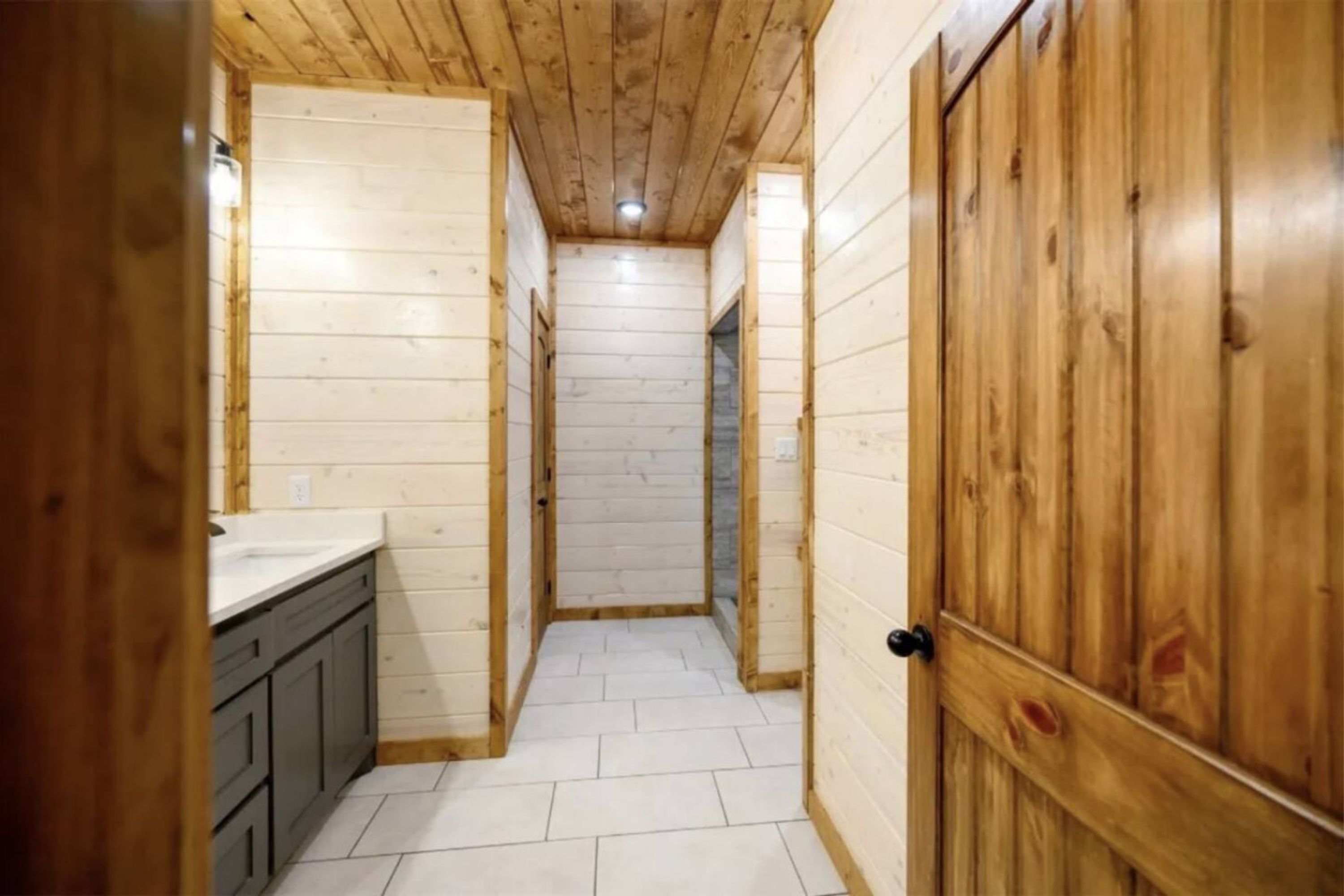 Un estrecho pasillo con paredes de madera y suelo de baldosas, que conduce a una puerta.