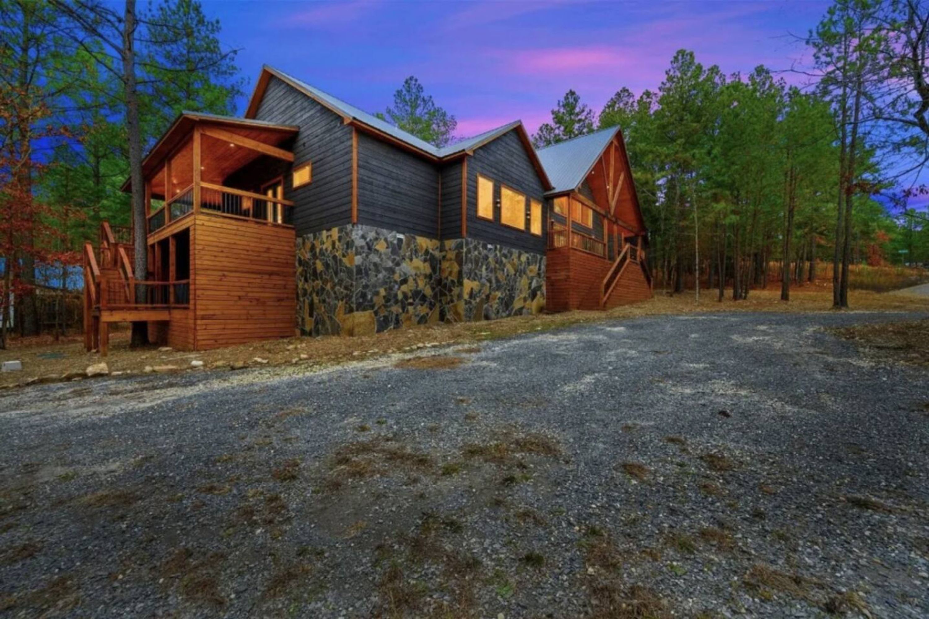 A cabin with a stone facade, wooden deck, and a gravel driveway.