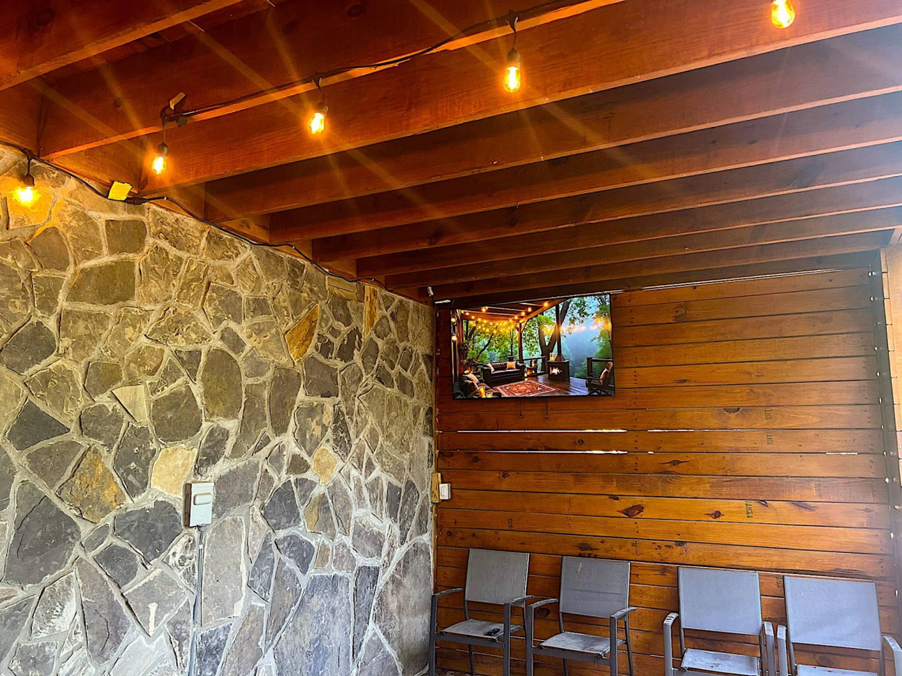 A stone wall, wooden ceiling, and a TV screen displaying an outdoor scene.