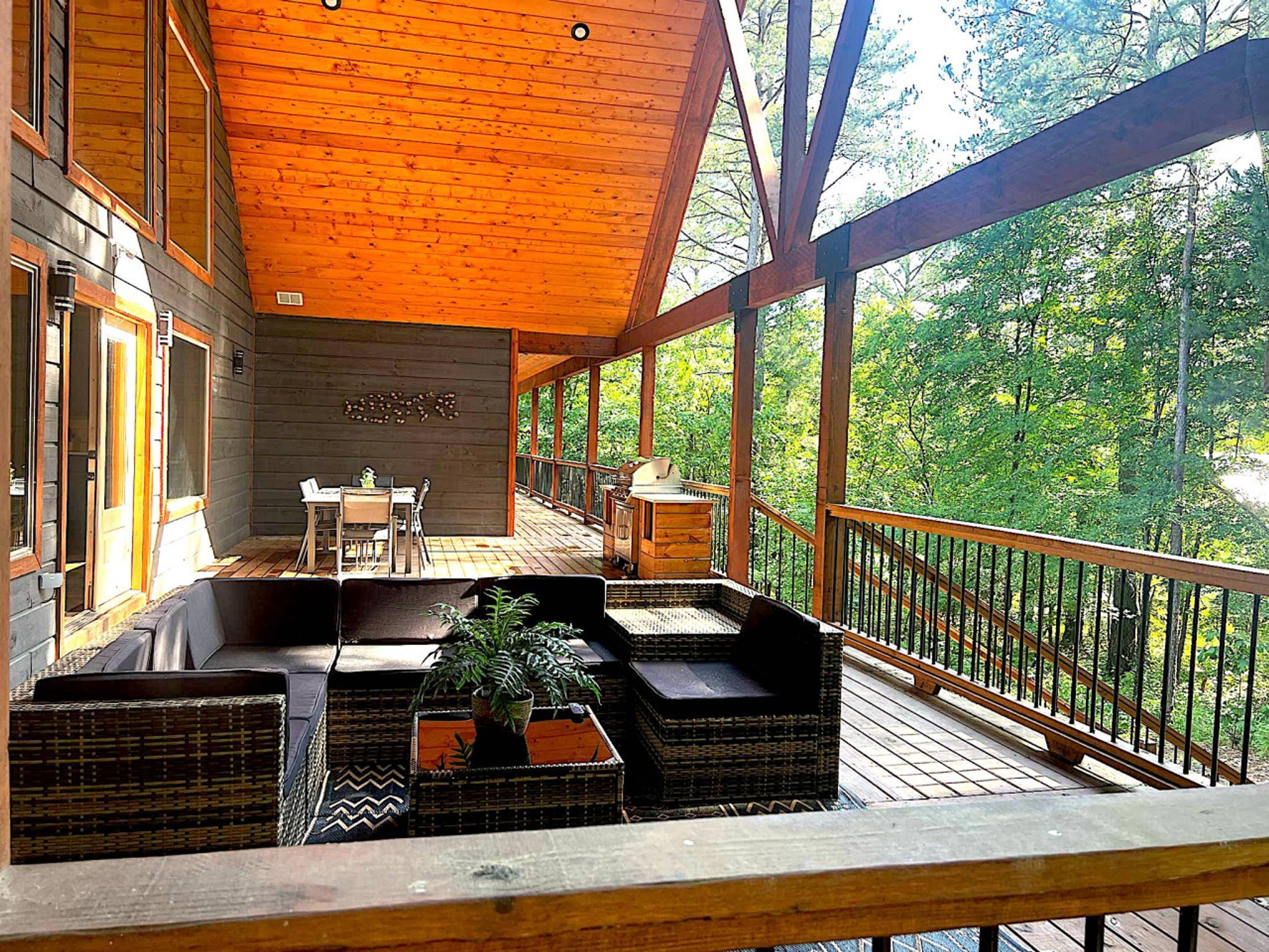 A wooden deck with outdoor seating, a dining area, and a view of a forest.
