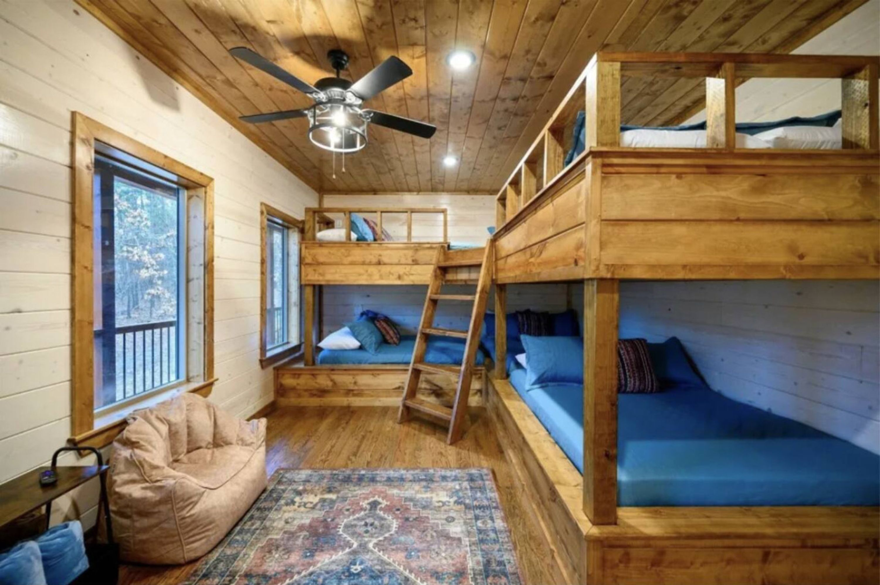 Ein gemütliches Blockhaus mit Holzwänden, Deckenventilator, Etagenbetten, einem Sitzsack und einem gemusterten Teppich.