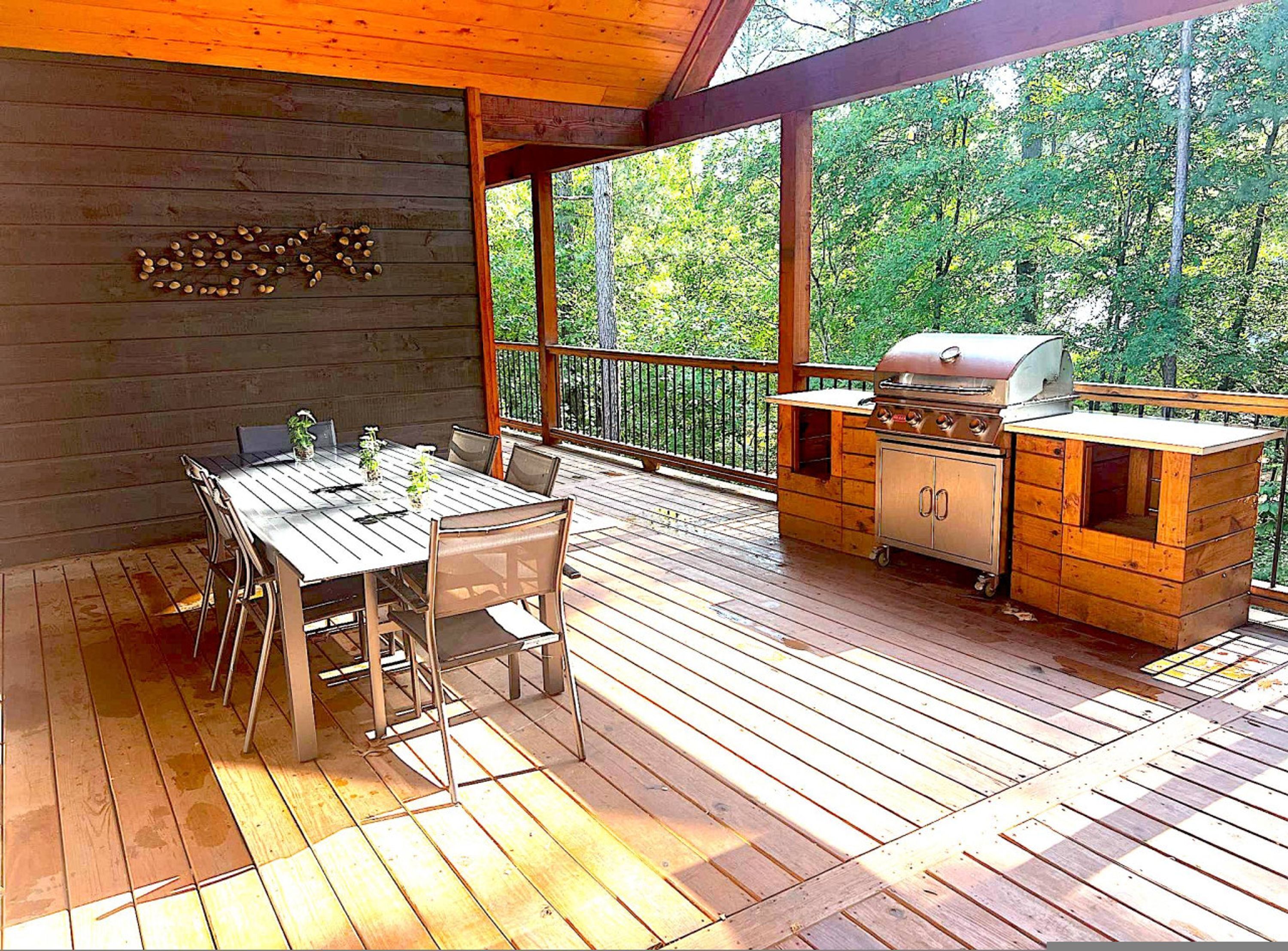 A wooden deck with a table and chairs, a grill, and a view of trees.