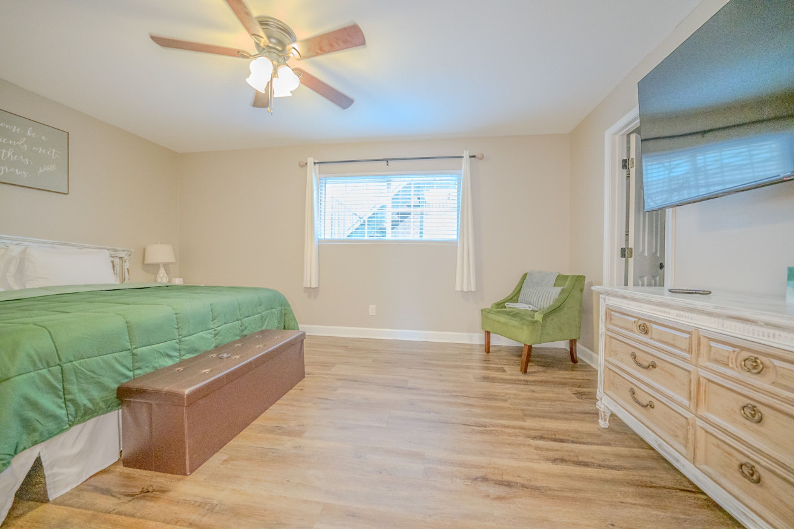 A bedroom with a bed, bench, dresser, and a ceiling fan.