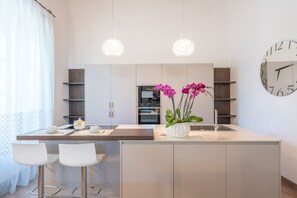 A modern kitchen with a central island, bar stools, pendant lights, and a clock on the wall. - Mery s House Elegant Apartment (Montepulciano)
