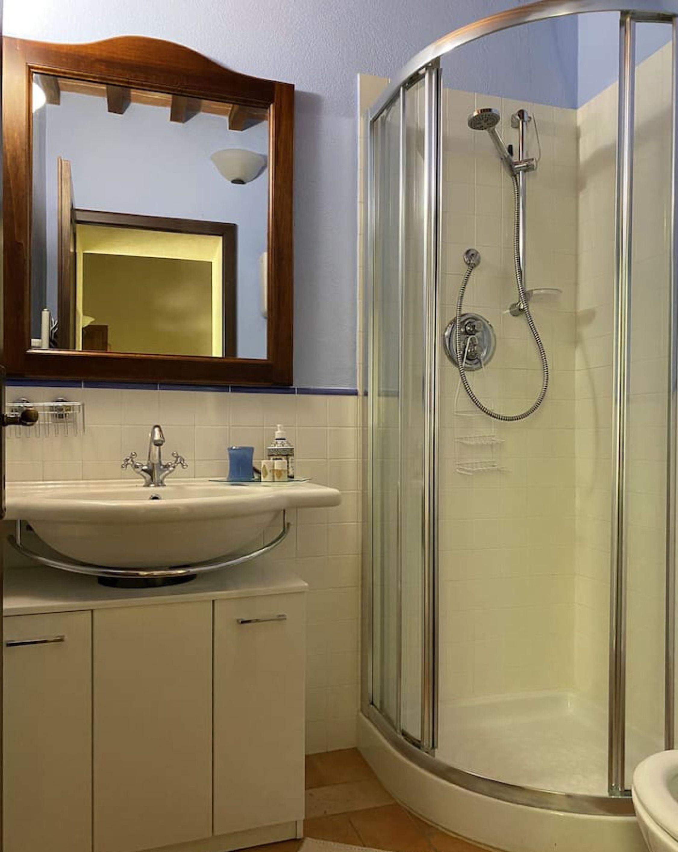 A bathroom with a glass-enclosed shower, a sink with a mirror above it, and white cabinets.