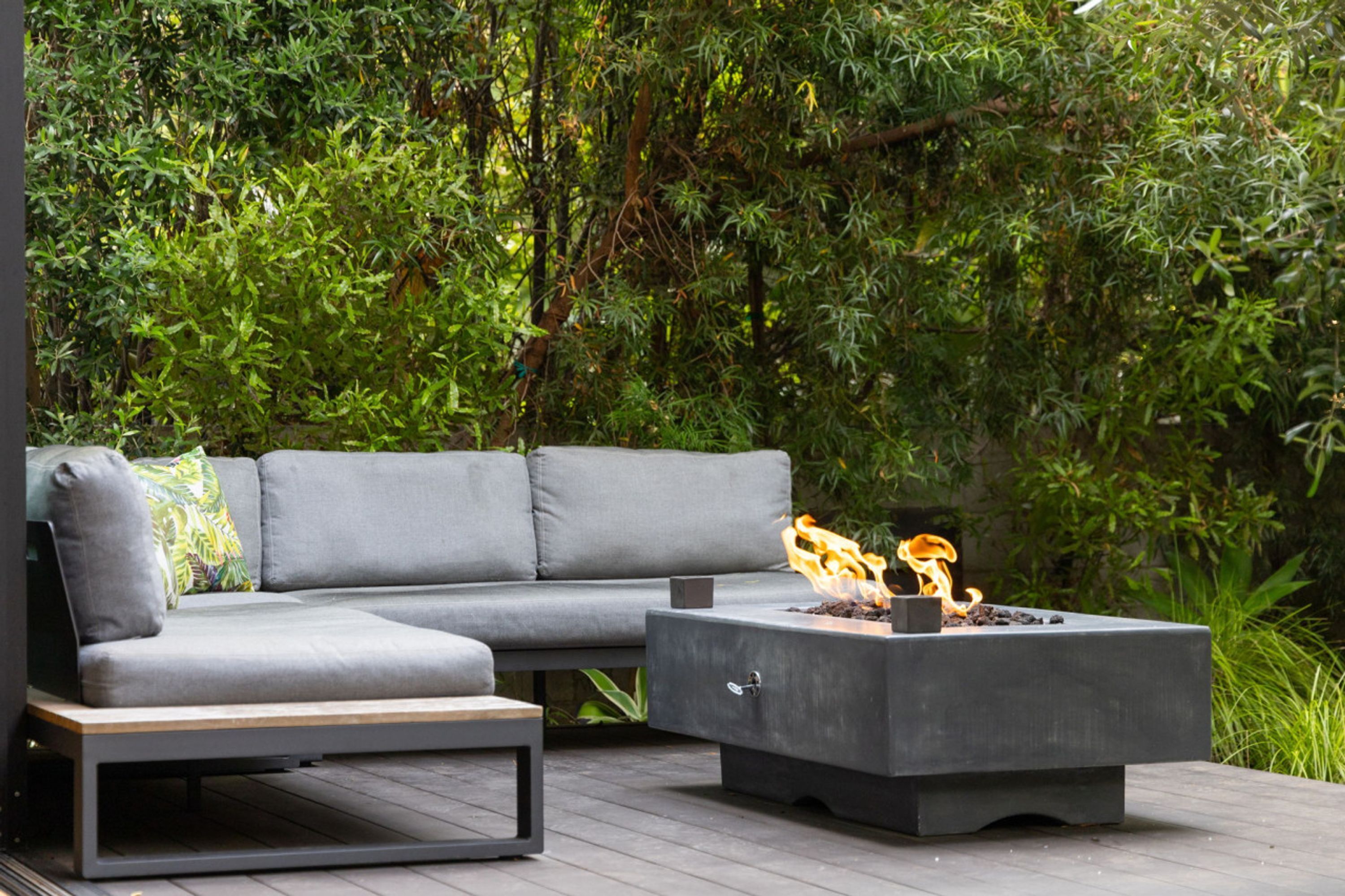 A modern outdoor seating area with a grey sofa and a square fire pit.