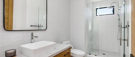 A modern bathroom with a white sink, wooden cabinets, a toilet, and a glass-enclosed shower area.