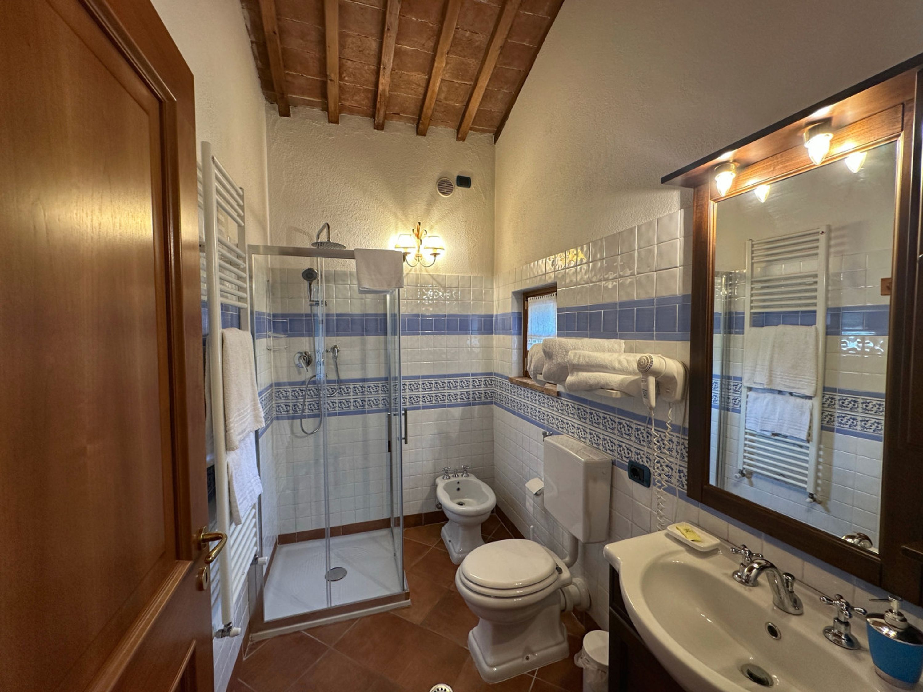 A bathroom with a shower, toilet, sink, and a mirror with lights.