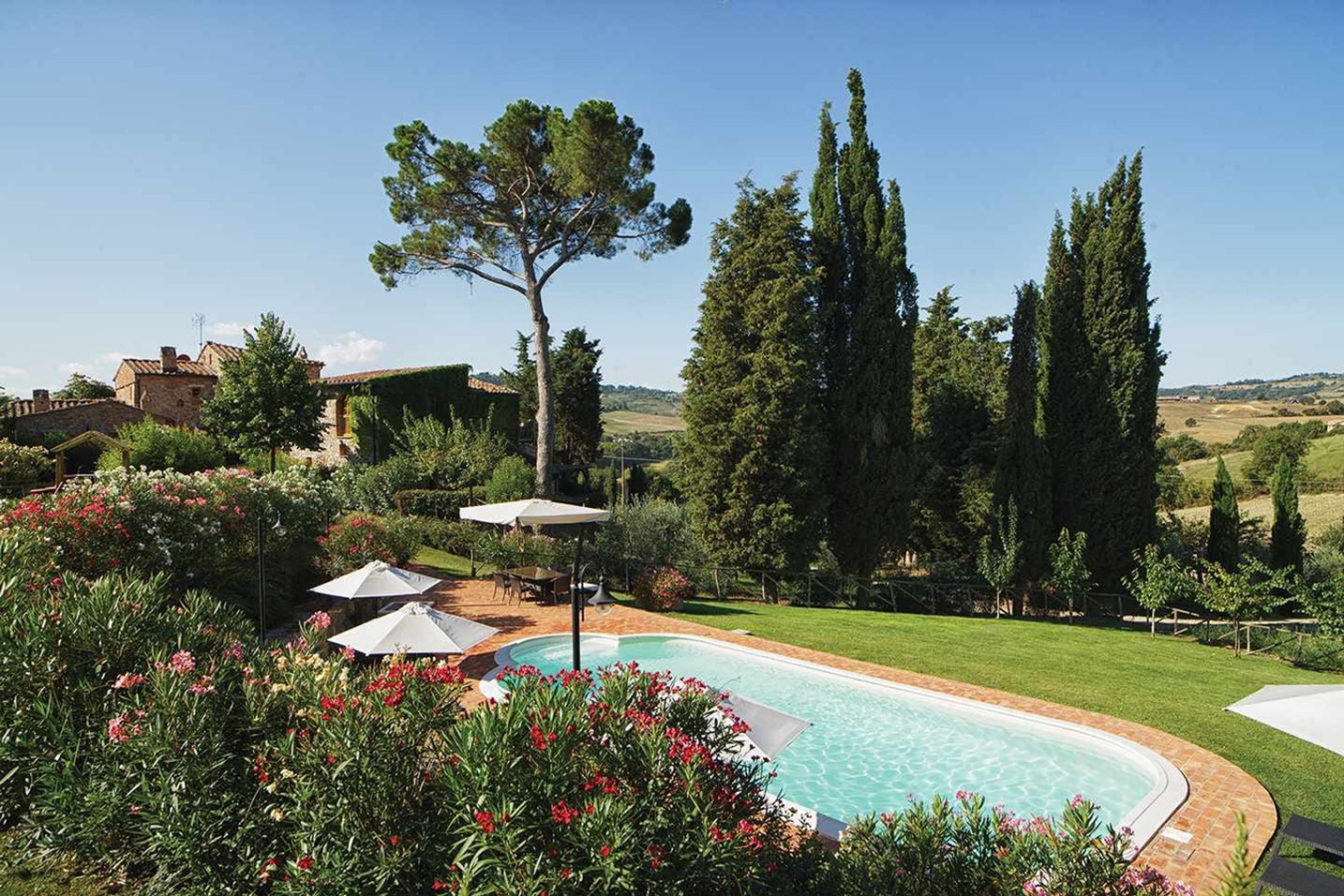 A swimming pool surrounded by lush greenery and tall trees, with a clear view of the countryside.