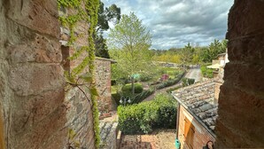 A view through a stone archway overlooking a courtyard with a tree, brick buildings, and a pathway. - Agriturismo Borgo 7 Tigli Apt 2 (Montepulciano)