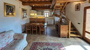 A rustic interior with exposed wooden beams, a dining area with wooden chairs, a kitchen with white cabinets, and a staircase. - Agriturismo Borgo 7 Tigli Apt 2 (Montepulciano)