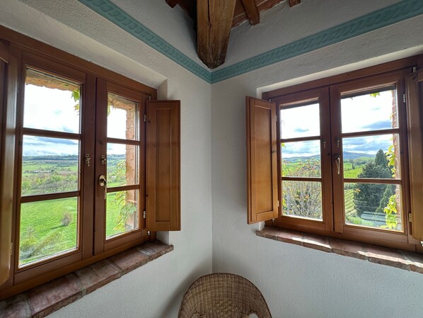 A room with two large windows offering views of a green landscape and distant hills.