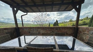 A covered outdoor dining area with a glass table and wicker chairs, overlooking a scenic landscape with hills and trees. - Agriturismo Borgo 7 Tigli Apt 2 (Montepulciano)