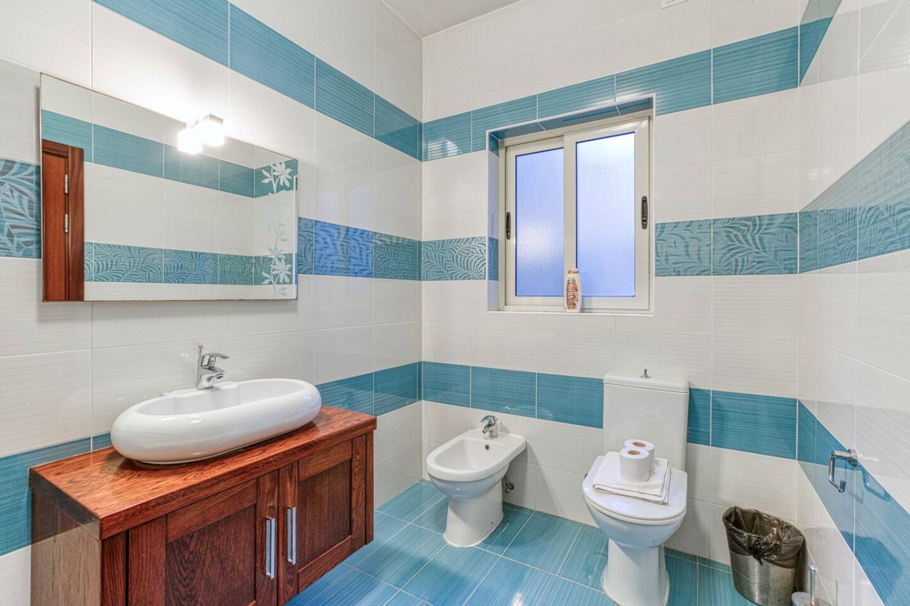 Ein Badezimmer mit einem Holzkosmetikschrank, einem Bidet, einer Toilette und einem Spiegel.