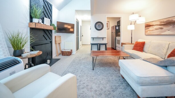 A modern living room with a white sofa, a coffee table, and a fireplace. There is a TV mounted on the wall and a painting above the sofa. - Top 3rd Floor Loft Resort Access No Elevator (Claysburg)