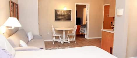 Una habitación de hotel con cama, una pequeña mesa con sillas, una lámpara y un cartel de 'Welcome' en la pared.