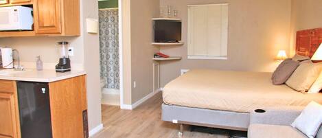Een kleine kamer met kitchenette, een bed, een televisie en een raam.