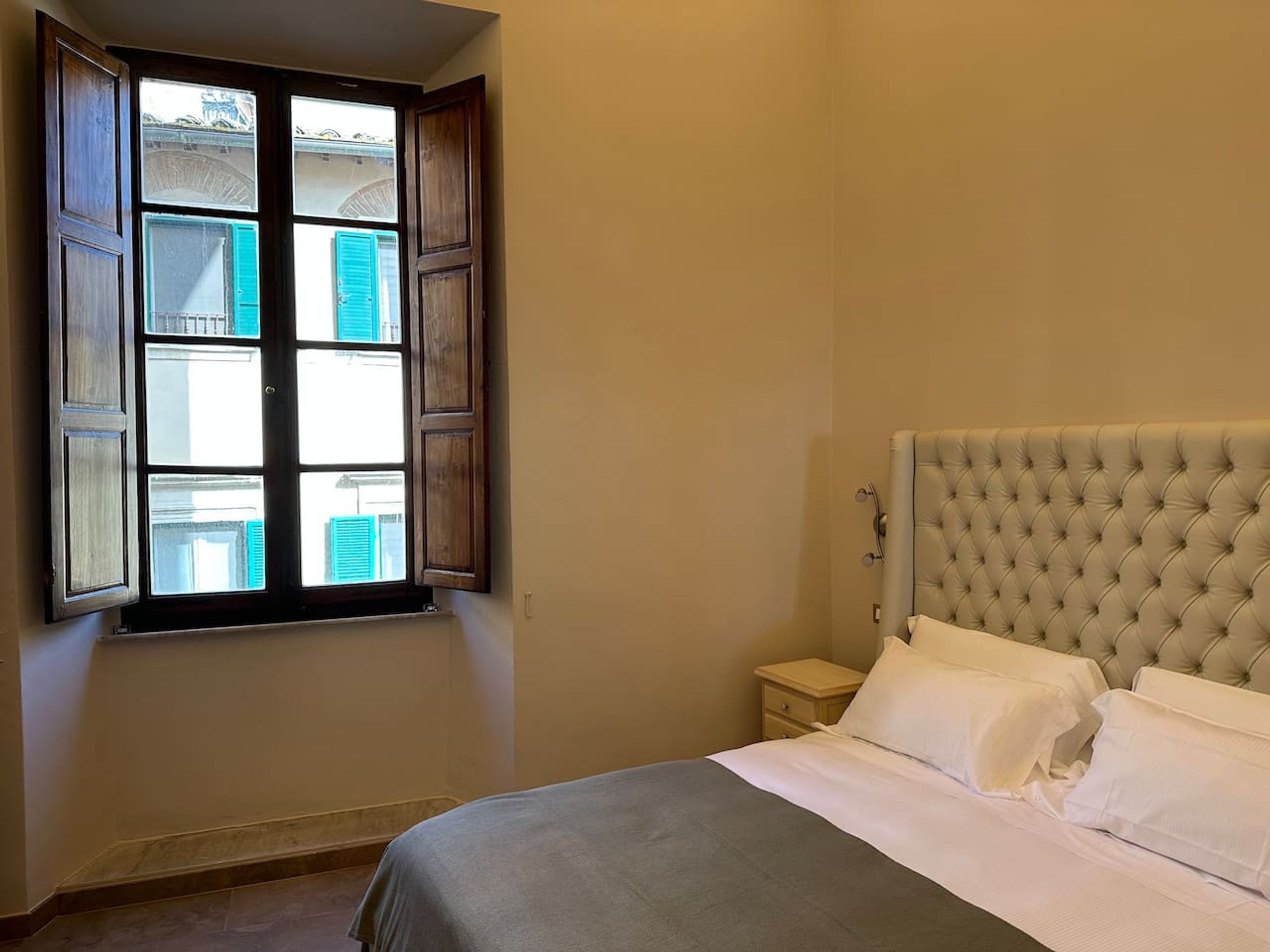 A bedroom with a bed, a nightstand, and a window with open shutters.