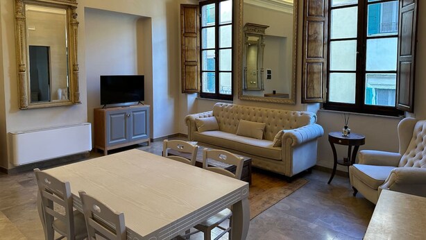A spacious living room with a large window, a television, and a dining area with chairs. - Tuscan Palace - Venturi Apartment (Montepulciano)