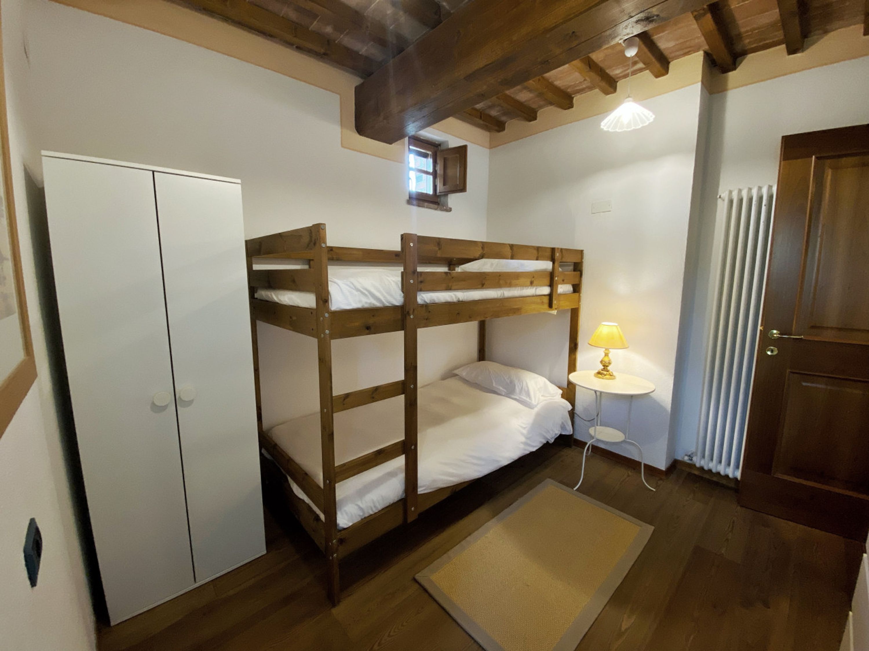 A bunk bed room with a wooden ceiling, a white wardrobe, a lamp, and a radiator.