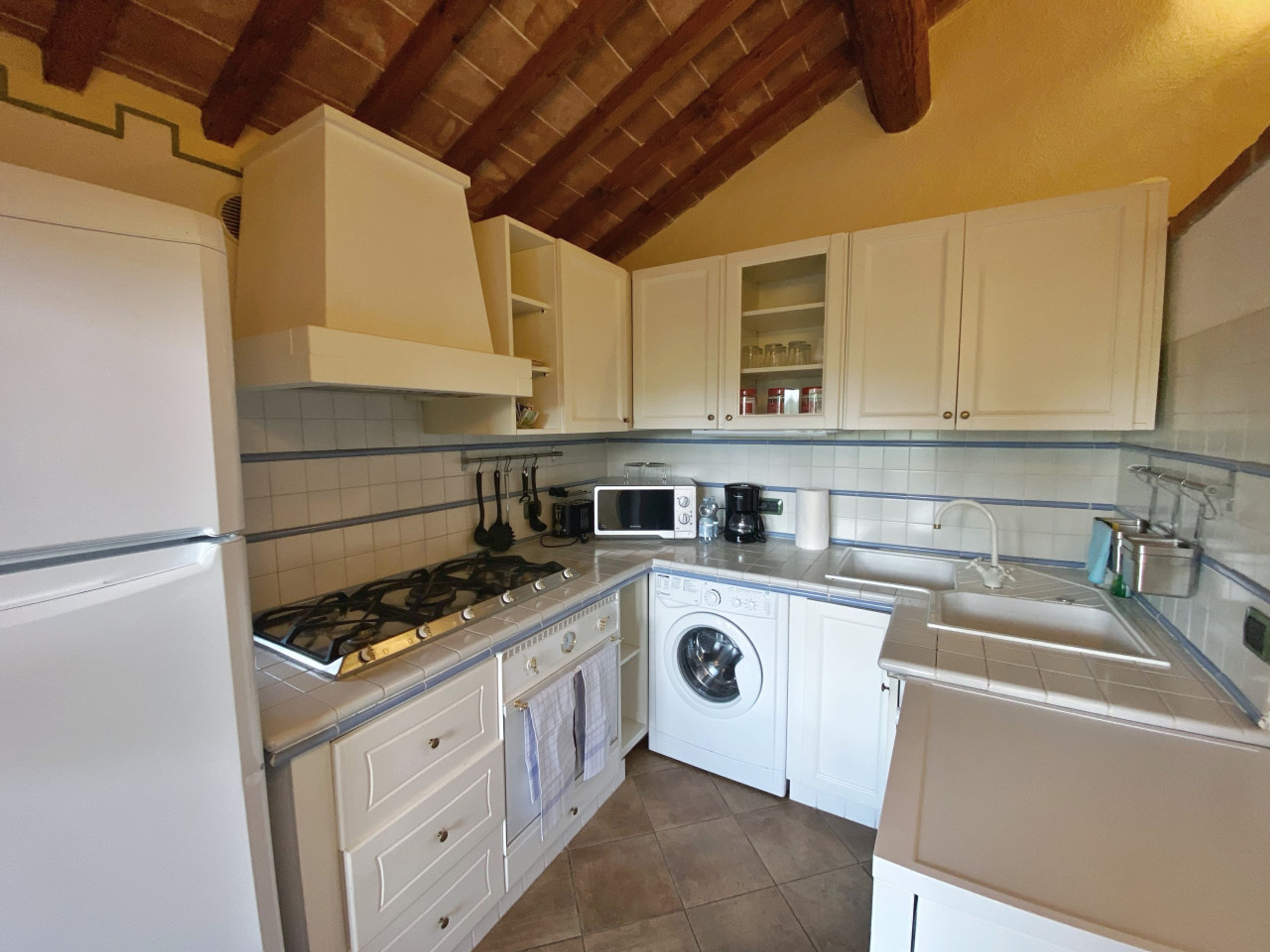 Une cuisine compacte avec des meubles blancs, une cuisinière à gaz, un four à micro-ondes, un lave-linge et un évier.