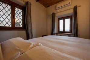 A bedroom with a large bed, a window with curtains, an air conditioning unit, and a radiator. - Tuscan Palace - Petit Apartment (Montepulciano)