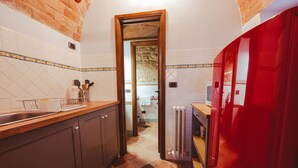 A kitchen with wooden cabinets, a tiled backsplash, and a red accent wall. - Tuscan Palace - Petit Apartment (Montepulciano)