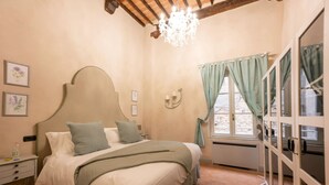 Une chambre à coucher comprenant un lit, une table de chevet, un lustre, une fenêtre avec des rideaux et une porte à panneaux de verre.