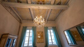 Une pièce dotée de décorations élaborées au plafond, d’un lustre et de grandes fenêtres ornées de rideaux verts.