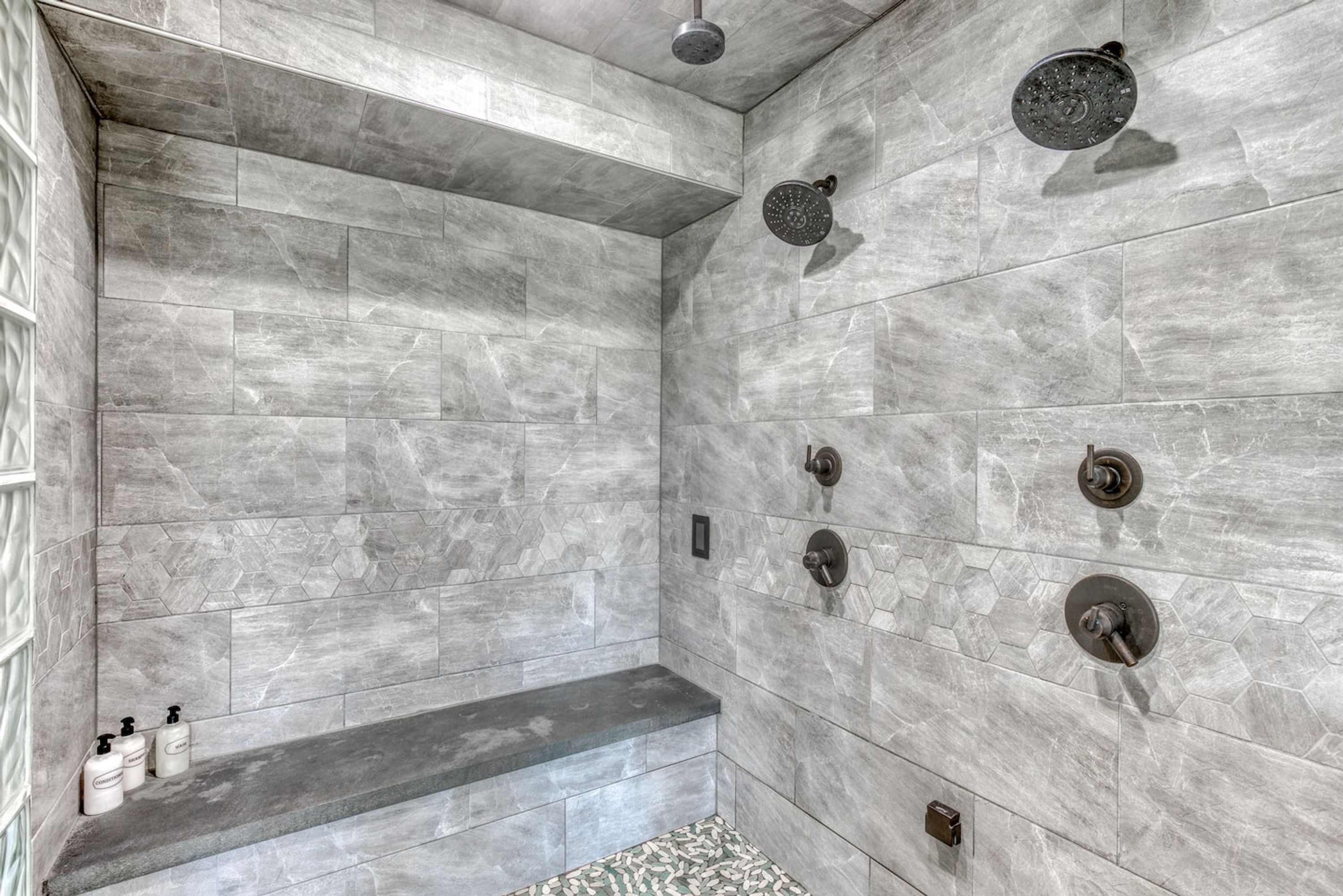Ducha moderna con azulejos grises e integrada una banca.