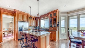 A spacious kitchen with wooden cabinets, a large island with bar stools, a built-in refrigerator, and a view to the outside. - Oceanfront Comfort Style Luxury Hot Tub Wifi 600 35 (Long Beach)