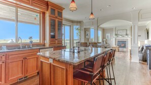 A spacious kitchen with wooden cabinets, a large island with bar stools, and a view of the outdoors. - Oceanfront Comfort Style Luxury Hot Tub Wifi 600 35 (Long Beach)
