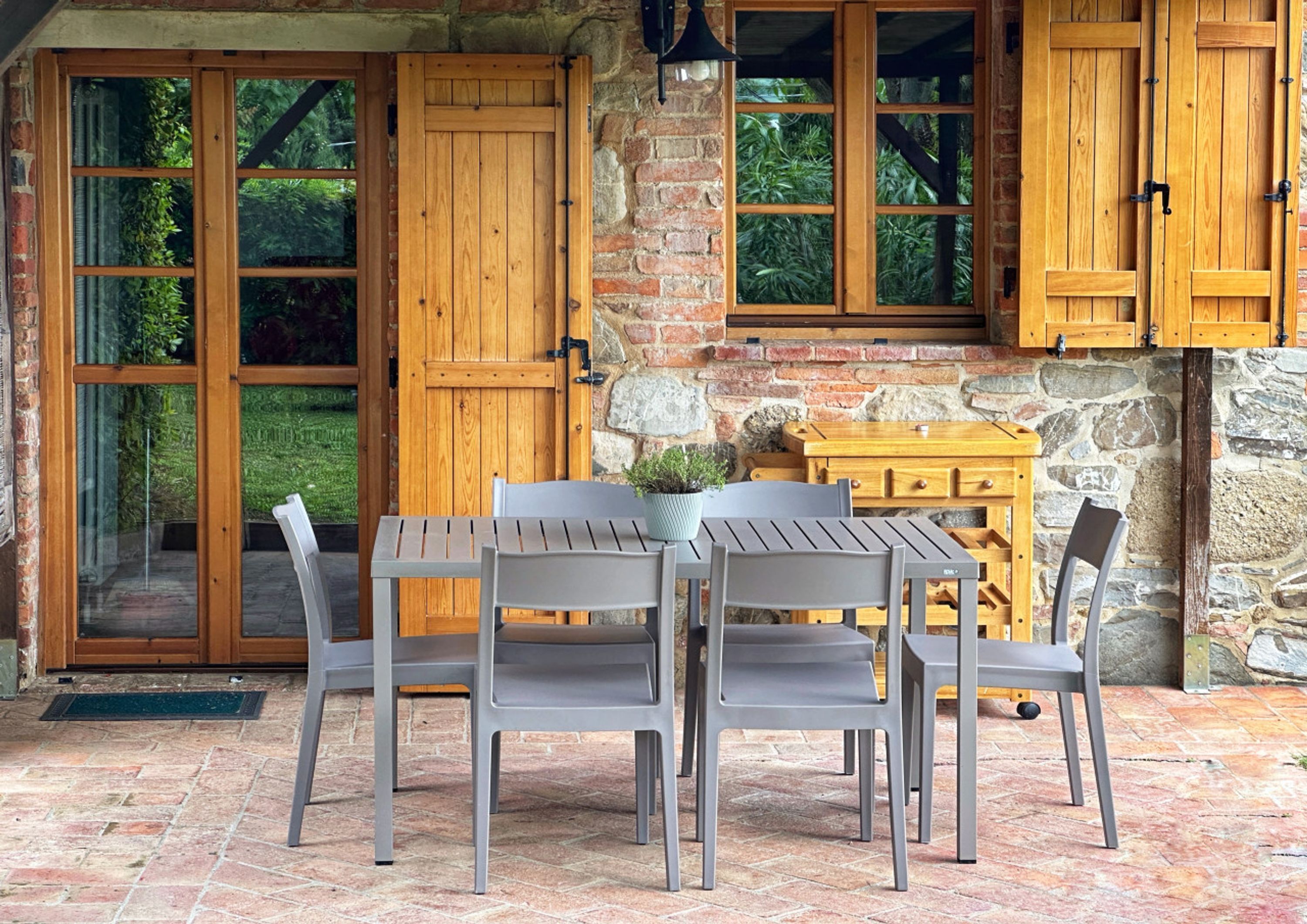 Een terras met een tafel, stoelen, houten deuren en een stenen muur.