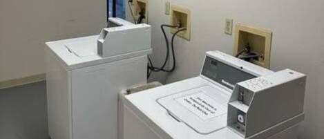 A laundry room with two washing machines and a dryer, a sign indicating the room is for laundry use, and electrical outlets on the wall.
