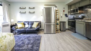 A compact living space with a sofa, a refrigerator, a microwave, and a small kitchen area. - Workspace Studio Ski-in Ski-out AC (Snowshoe)
