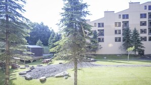 A building with multiple windows and a grassy courtyard with trees and rocks. - Workspace Studio Ski-in Ski-out AC (Snowshoe)