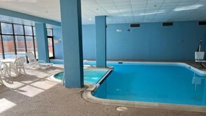 An indoor swimming pool with a blue tiled floor, white lounge chairs, and a ceiling with a grid pattern. - Workspace Studio Ski-in Ski-out AC (Snowshoe)