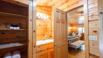 A wooden cabin interior with a bathroom featuring a sink, mirror, and towel storage.