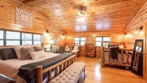 A log cabin bedroom with a large bed, a bench, a desk, and a chair.