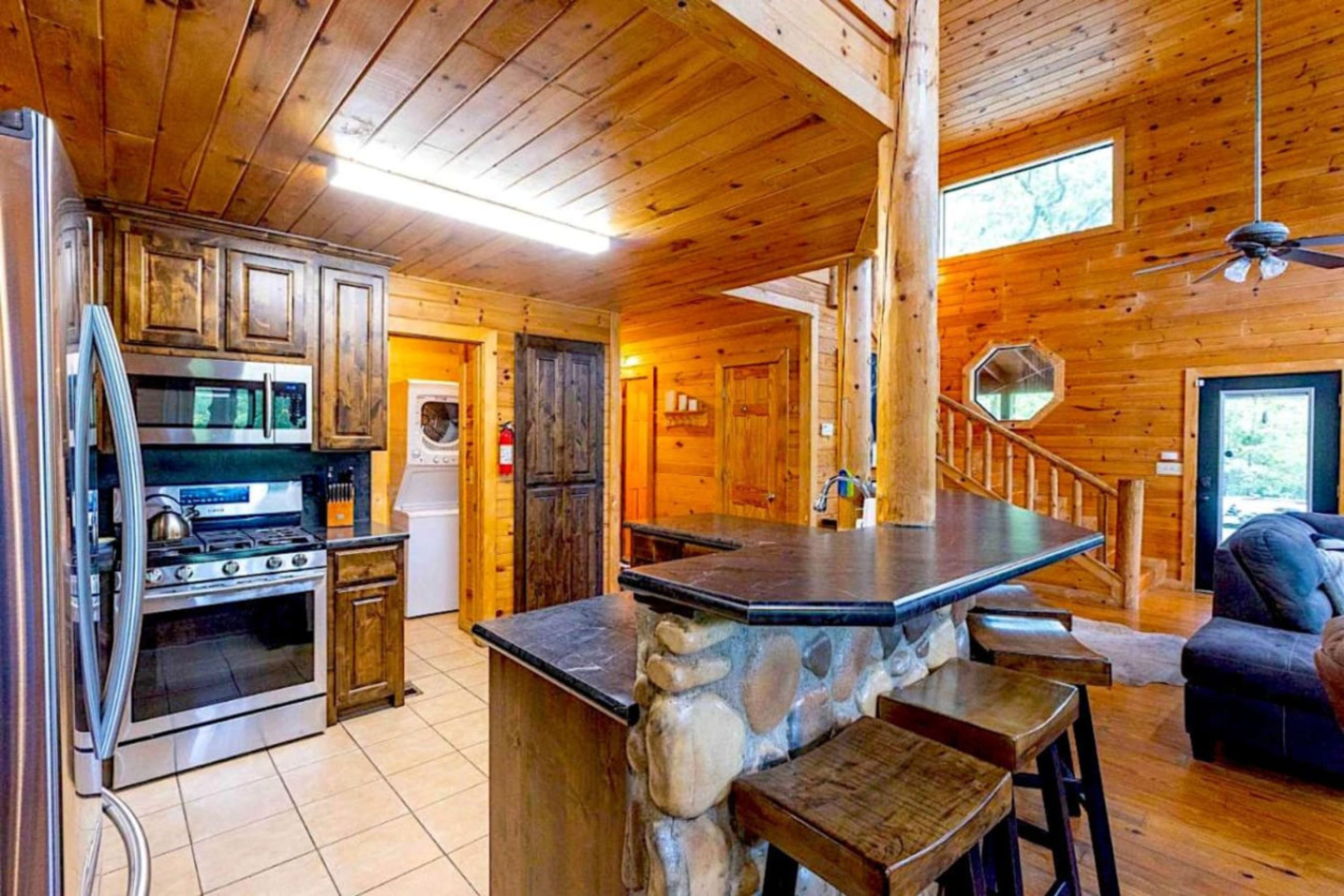 A cabin interior with a kitchen, stone bar, and wooden staircase.