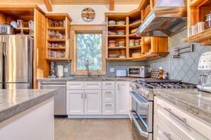 A modern kitchen with white cabinets, stainless steel appliances, and wooden shelves with glassware. - Boutique Cabin Design Luxury Hot Tub Path to Beach (Long Beach)