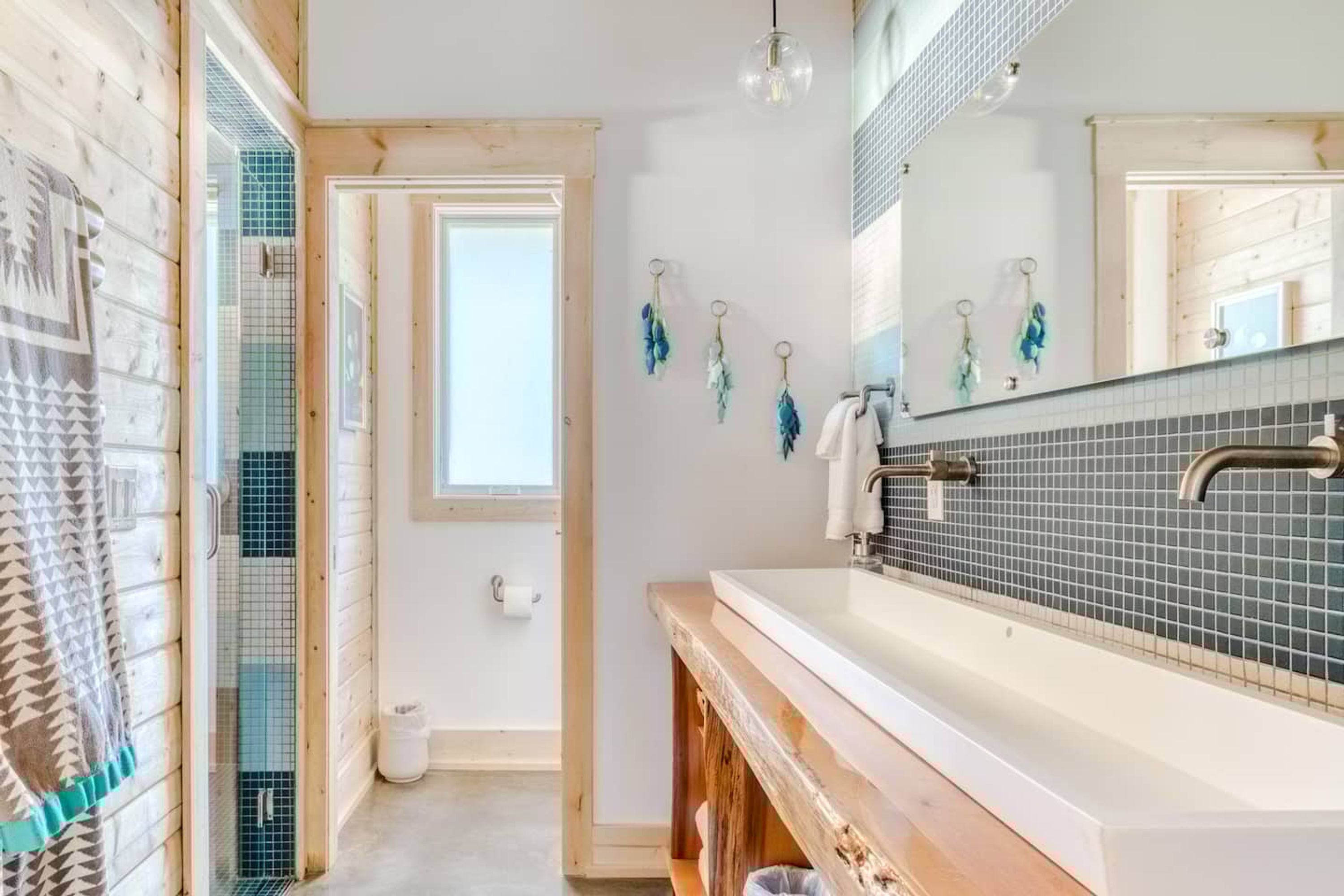 Un baño con tocador de madera, un espejo grande y zona de ducha con puerta de cristal.