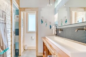 A bathroom with a wooden vanity, a large mirror, and a shower area with a glass door. - Boutique Cabin Design Luxury Hot Tub Path to Beach (Long Beach)