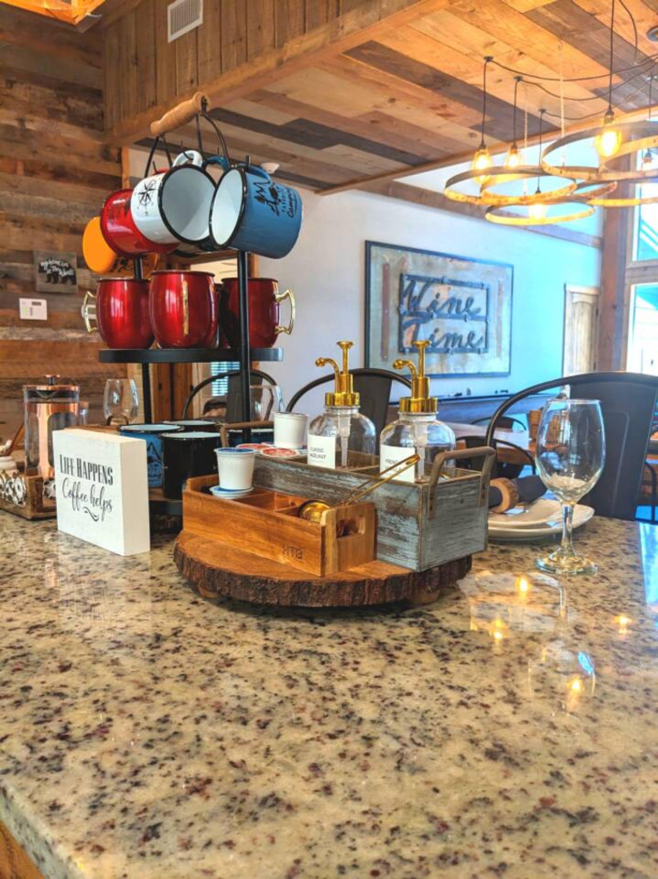 Una encimera de cocina con una estación de café, que incluye una bandeja con tazas de café, un cartel con la inscripción 'Life Happens Coffee Helps' y un soporte de madera para tazas.