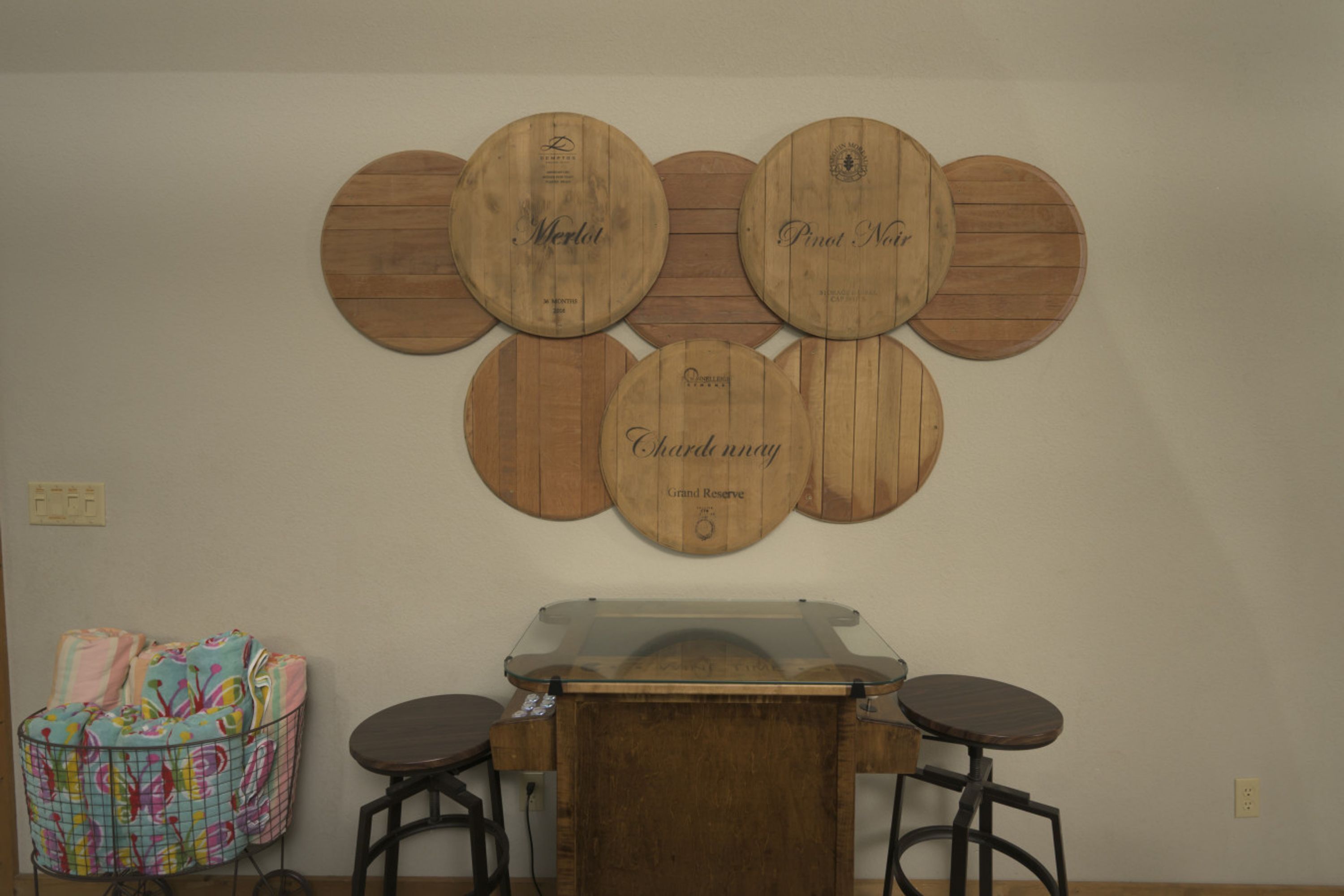 A bar area with a wooden bar counter and stools, a decorative wall with wine barrel labels, and a colorful storage unit.